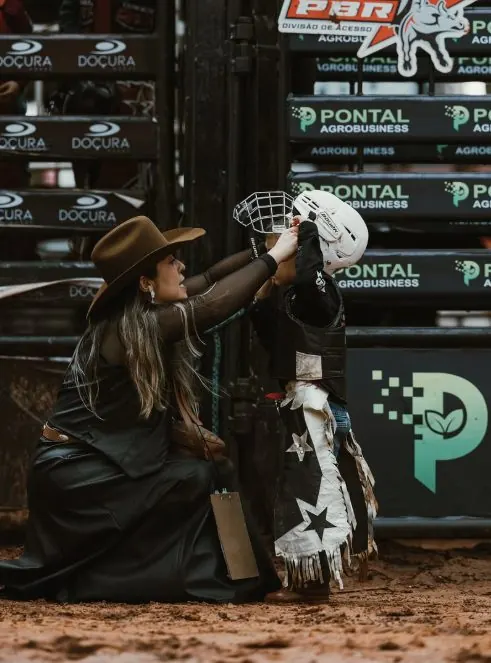Mulher de chapéu ajustando o capacete de uma criança antes do rodeio
